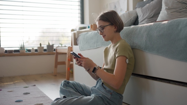 Diabetic girl with CGM sensor checking her blood sugar level in app.