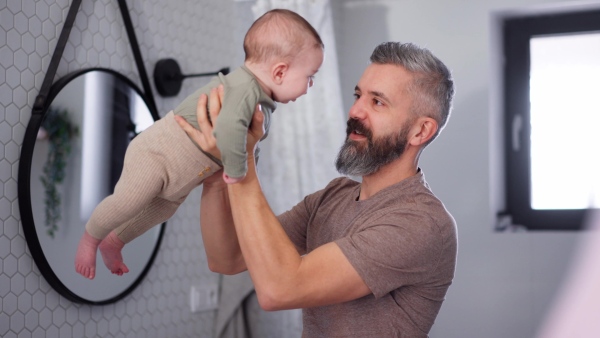A father with his baby son in bathroom, holding him in arms and playing with him.