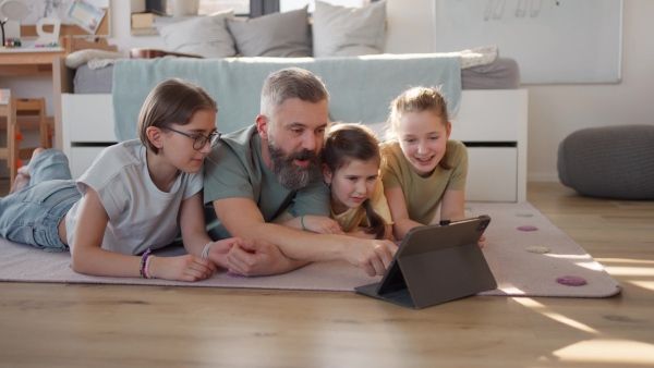 Video of father with three daughters watching tv show on tablet. Girl dad concept.