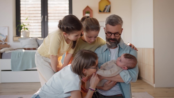Three sisters looking at newborn brother in fathers arms. Big family concept.