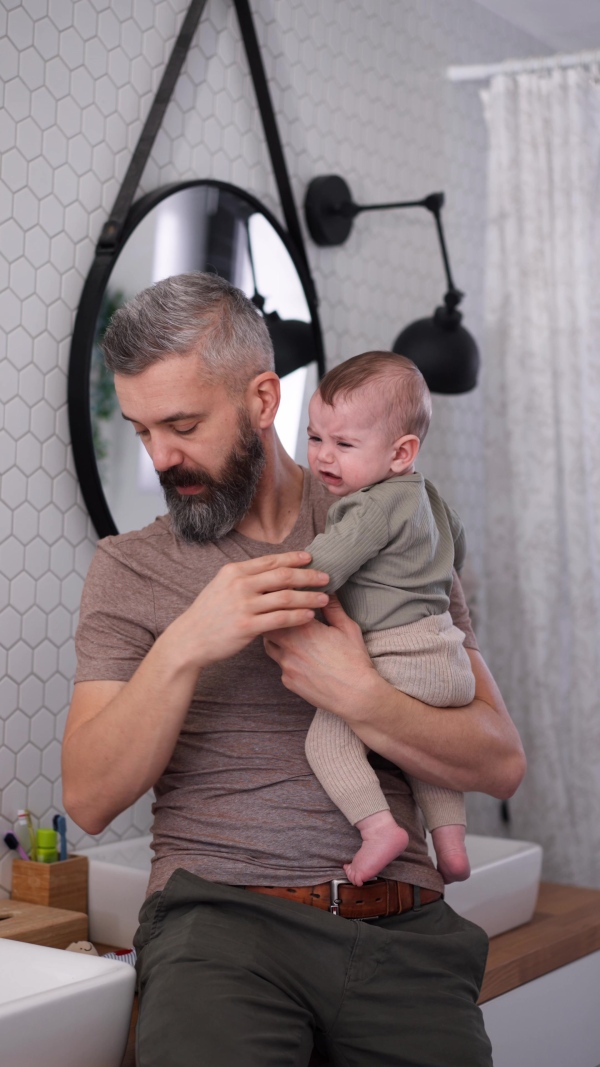 Father comforting his crying baby son, holding him in arms.