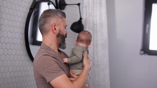 A father with his baby son in bathroom, holding him in arms and playing with him.