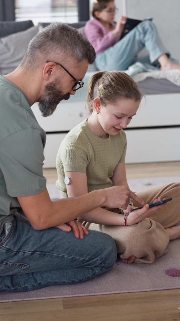 Diabetic girl with a CGM sensor on her arm. Father using an app to monitor blood sugar levels.
