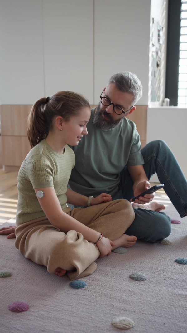 Diabetic girl with a CGM sensor on her arm. Father using an app to monitor blood sugar levels.