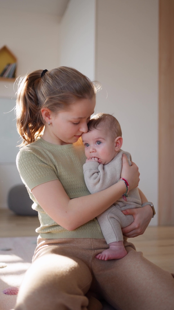 Big sister comforting sad baby brother, holding him in arms.