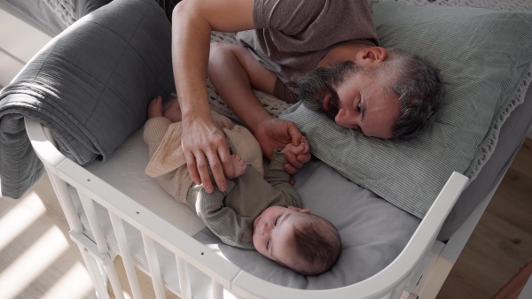 Father putting the baby to sleep, lying next to him in the crib and soothing him.
