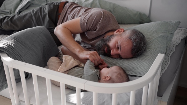 Father putting the baby to sleep, lying next to him in the crib and soothing him.