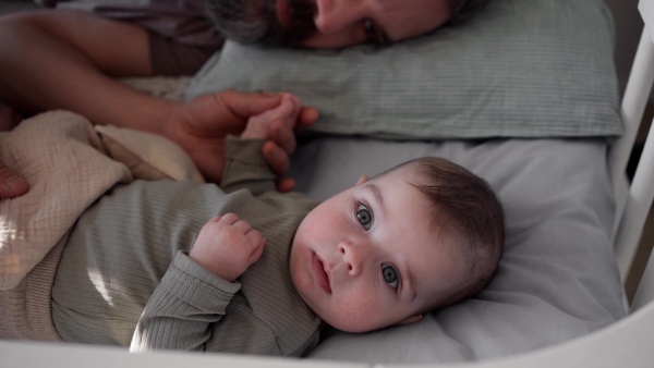Father putting the baby to sleep, lying next to him in the crib and soothing him.