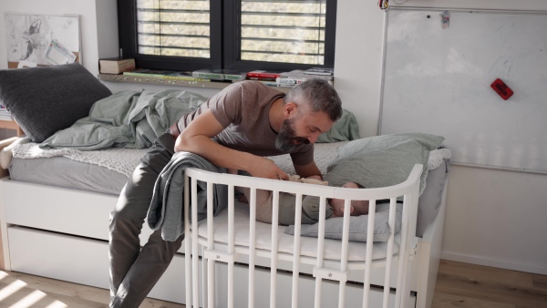 Father putting the baby to sleep, lying next to him in the crib and soothing him.