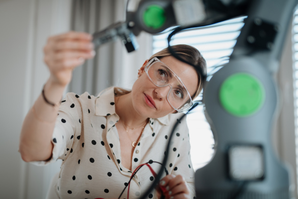Female engineer building and programming a robotic arm at home. Robotics concept.