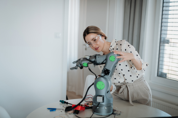 Female engineer building and programming a robotic arm at home. Robotics concept.