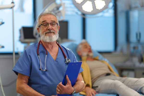 Portrait of older doctor standing in examination room in hospital.