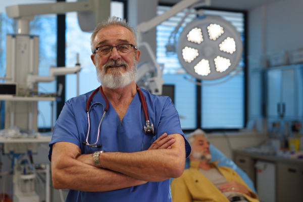 Portrait of older doctor standing in examination room in hospital.