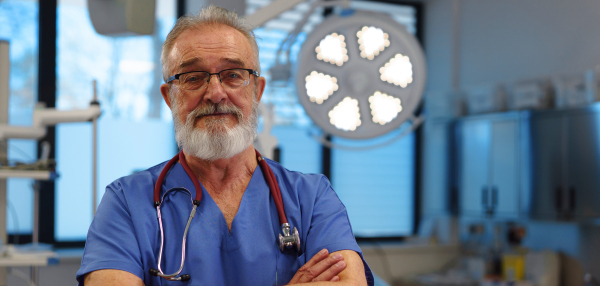 Portrait of older doctor standing in examination room in hospital. Banner with copy space.