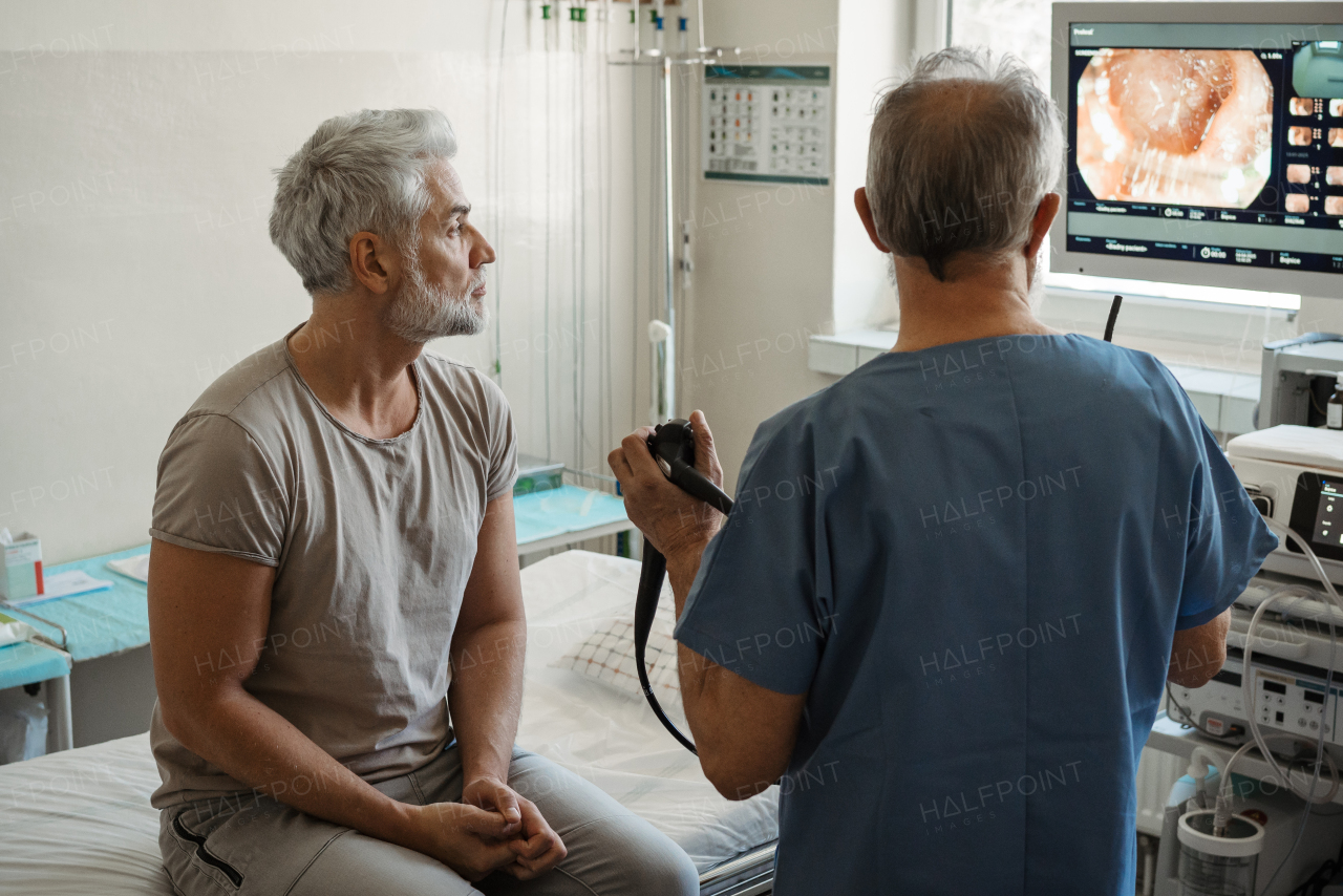 Doctor explaining colonoscopy results to patient using monitor images on screen.