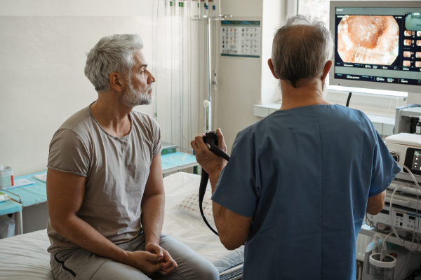 Doctor explaining colonoscopy results to patient using monitor images on screen.