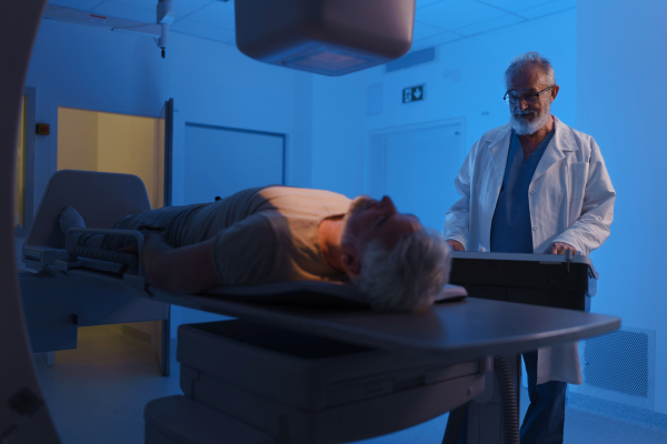 Male patient undergoing X-ray examination using a tilting radiographic wall stand.