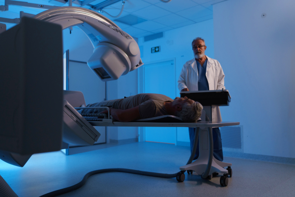 Male patient undergoing X-ray examination using a tilting radiographic wall stand.