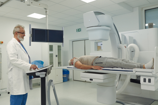 Male patient undergoing X-ray examination using a tilting radiographic wall stand.