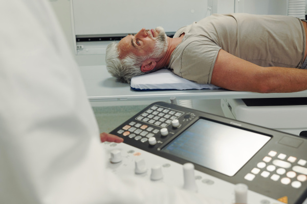 Male patient undergoing X-ray examination using a tilting radiographic wall stand.