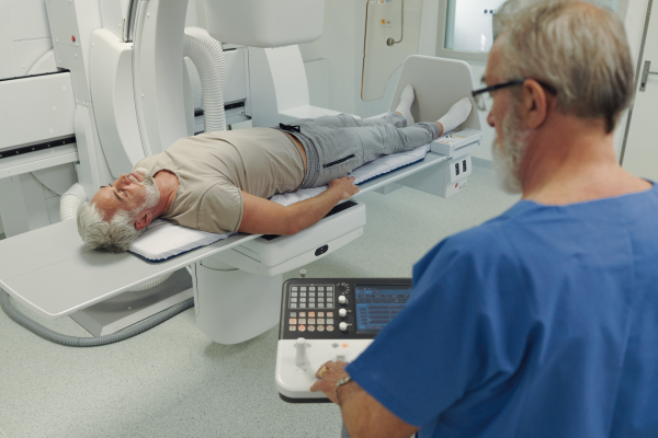 Male patient undergoing X-ray examination using a tilting radiographic wall stand.