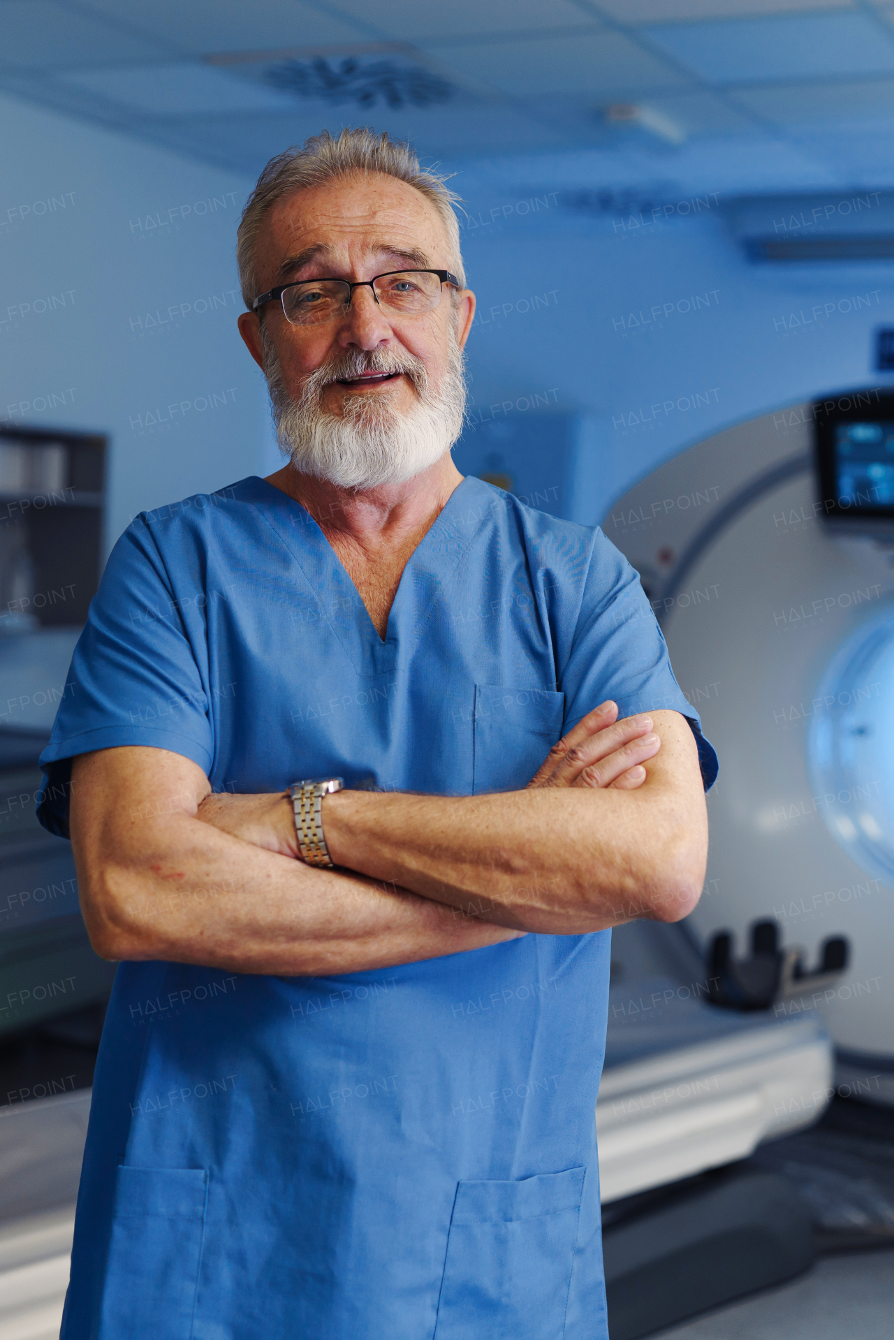 Medical specialist standing by CT scanner, looking at camera in hospital setting.
