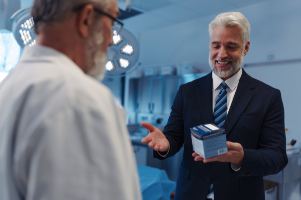 Medical sales representative presenting new medication to doctors, standing in examination room. Hospital setting.