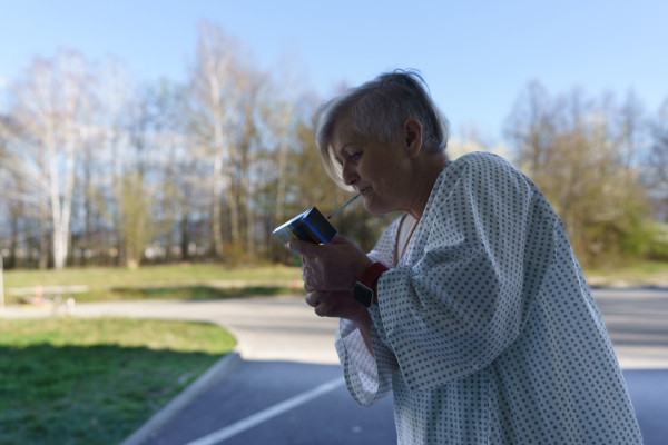 Female patient in hospital gown smoking outside medical facility.