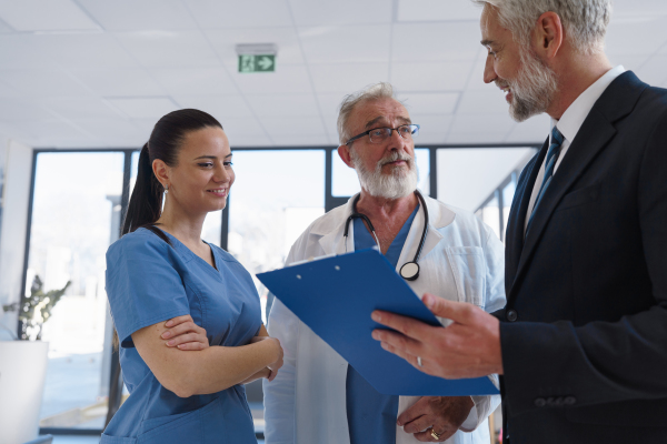 Medical sales representative presenting new medication to doctors, standing hospital hallway. Hospital setting.