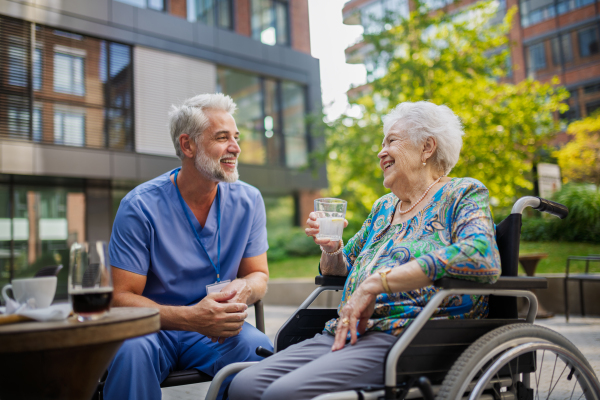 Male nurse having a cup of coffee with senior patient in a wheelchair at a cafe.