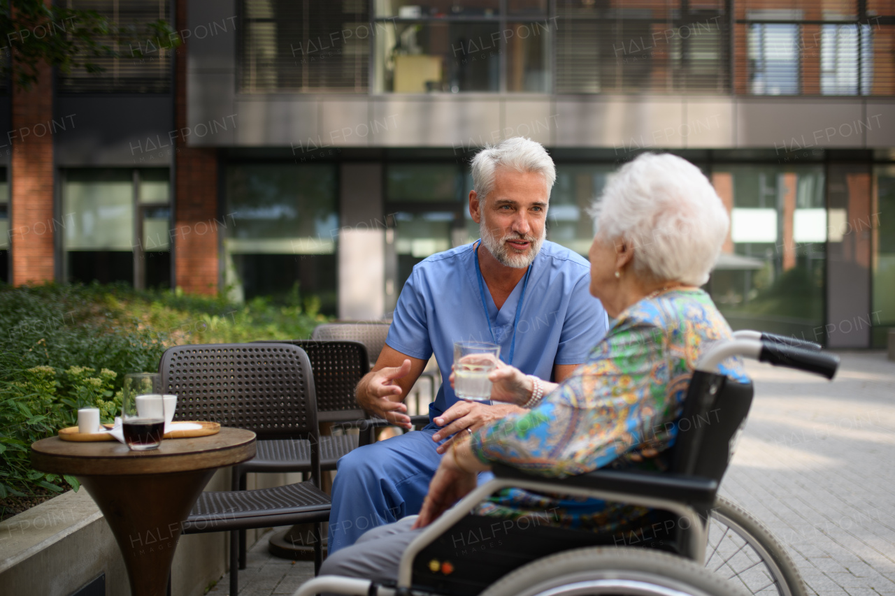Male nurse having a cup of coffee with senior patient in a wheelchair at a cafe.
