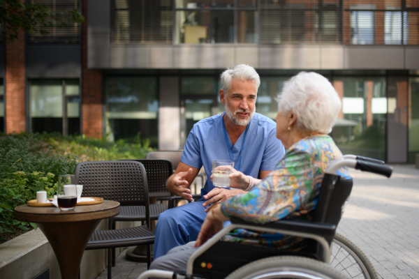 Male nurse having a cup of coffee with senior patient in a wheelchair at a cafe.