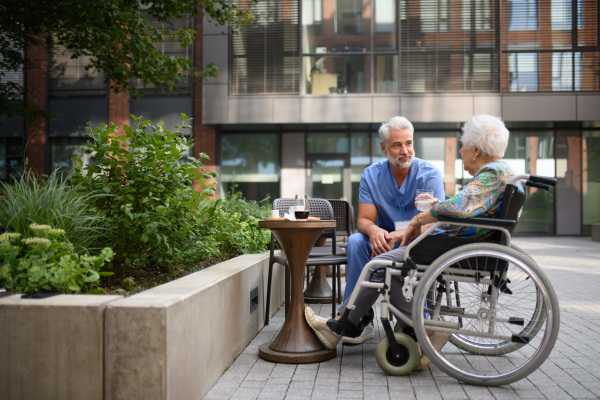 Male nurse having a cup of coffee with senior patient in a wheelchair at a cafe.