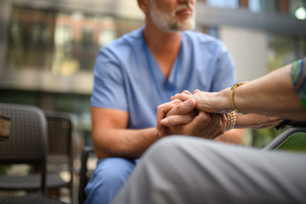 Close up of holding hands of male healthcare worker and senior patient.