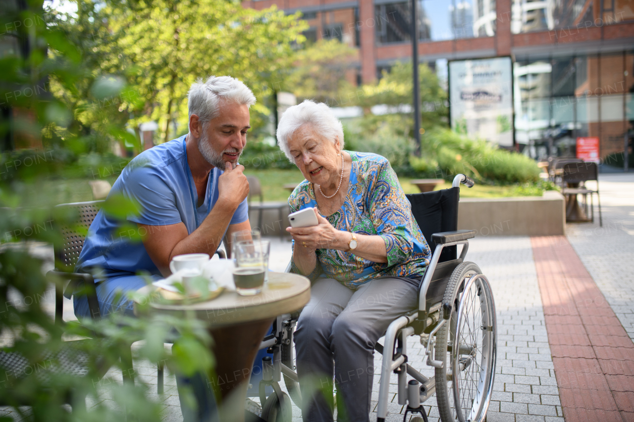 Male nurse having a cup of coffee with senior patient in a wheelchair at a cafe.