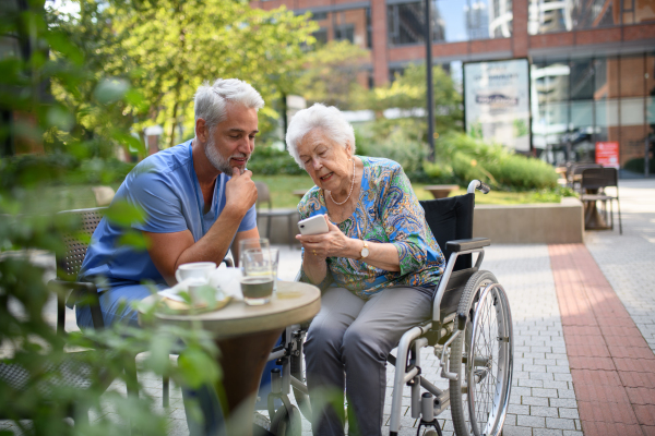 Male nurse having a cup of coffee with senior patient in a wheelchair at a cafe.