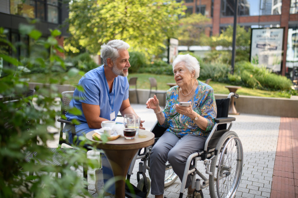 Male nurse having a cup of coffee with senior patient in a wheelchair at a cafe.
