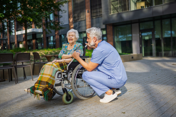 Male caregiver pushing senior woman in a wheelchair.