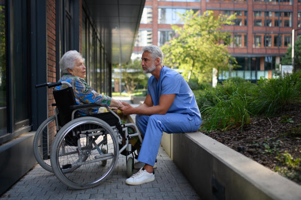 Male caregiver reading book to senior woman in a wheelchair.
