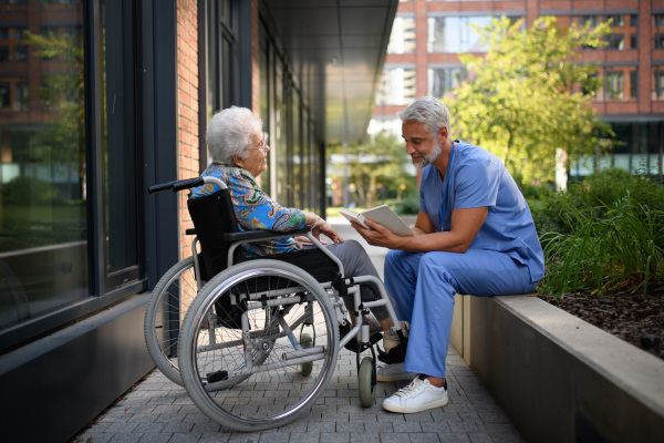 Male caregiver reading book to senior woman in a wheelchair.