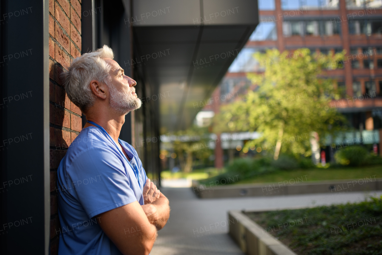 Frustrated and burnt-out doctor sitting outside the hospital, feeling down. Mental health problems.