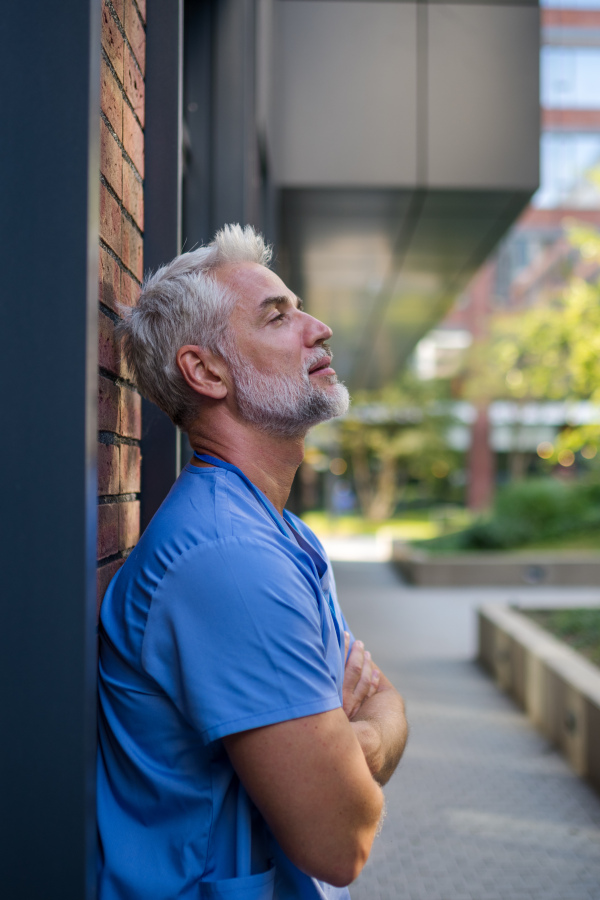 Frustrated and burnt-out doctor standing outside the hospital, feeling down. Mental health problems.