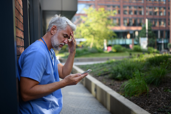 Frustrated and burnt-out doctor standing outside the hospital, feeling down. Mental health problems.