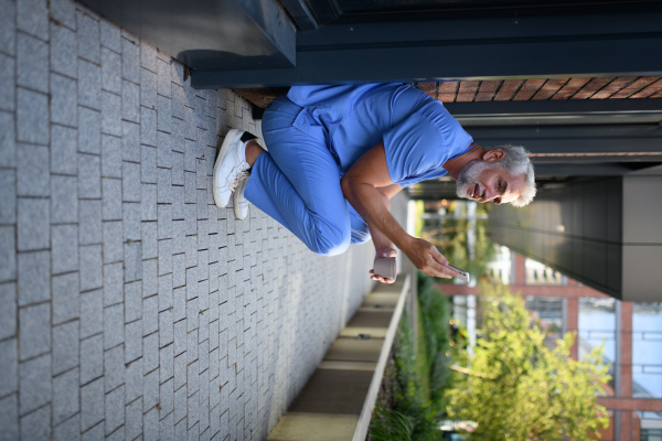 Healthcare worker in scrubs sitting outside hospital and checking phone during break.