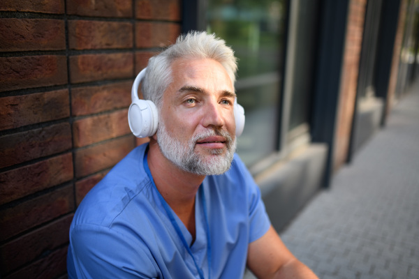 Healthcare worker relaxing with music outside hospital, headphones on head.