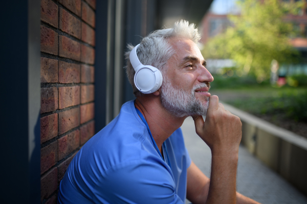 Healthcare worker relaxing with music outside hospital, headphones on head.