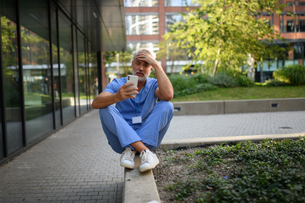 Frustrated and burnt-out doctor standing outside the hospital, feeling down. Mental health problems.