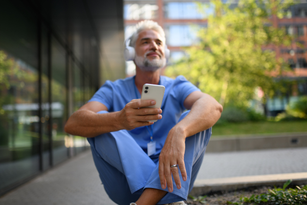 Healthcare worker relaxing with music outside hospital, headphones on head.