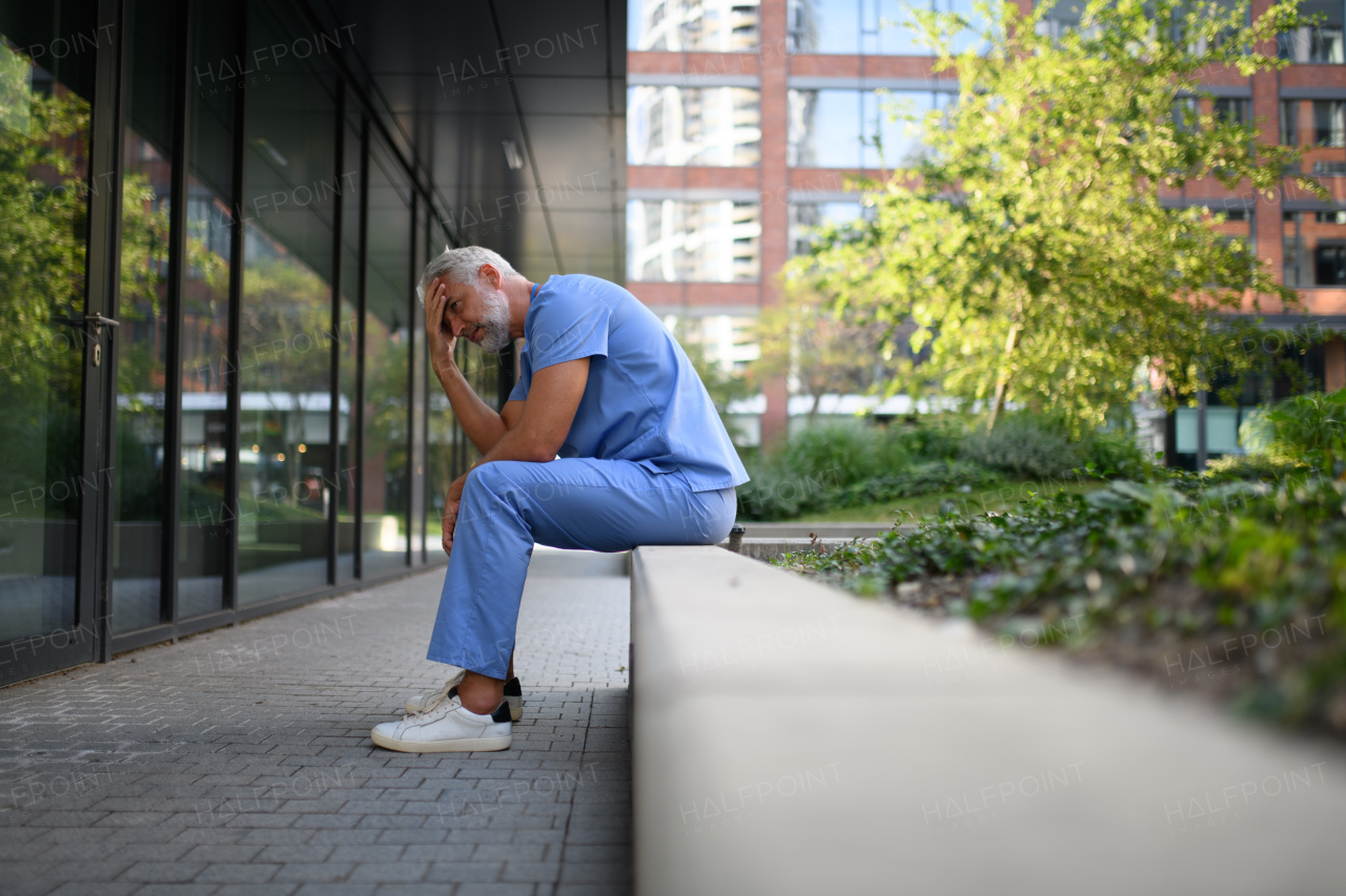 Frustrated and burnt-out doctor sitting outside the hospital, feeling down. Mental health problems.