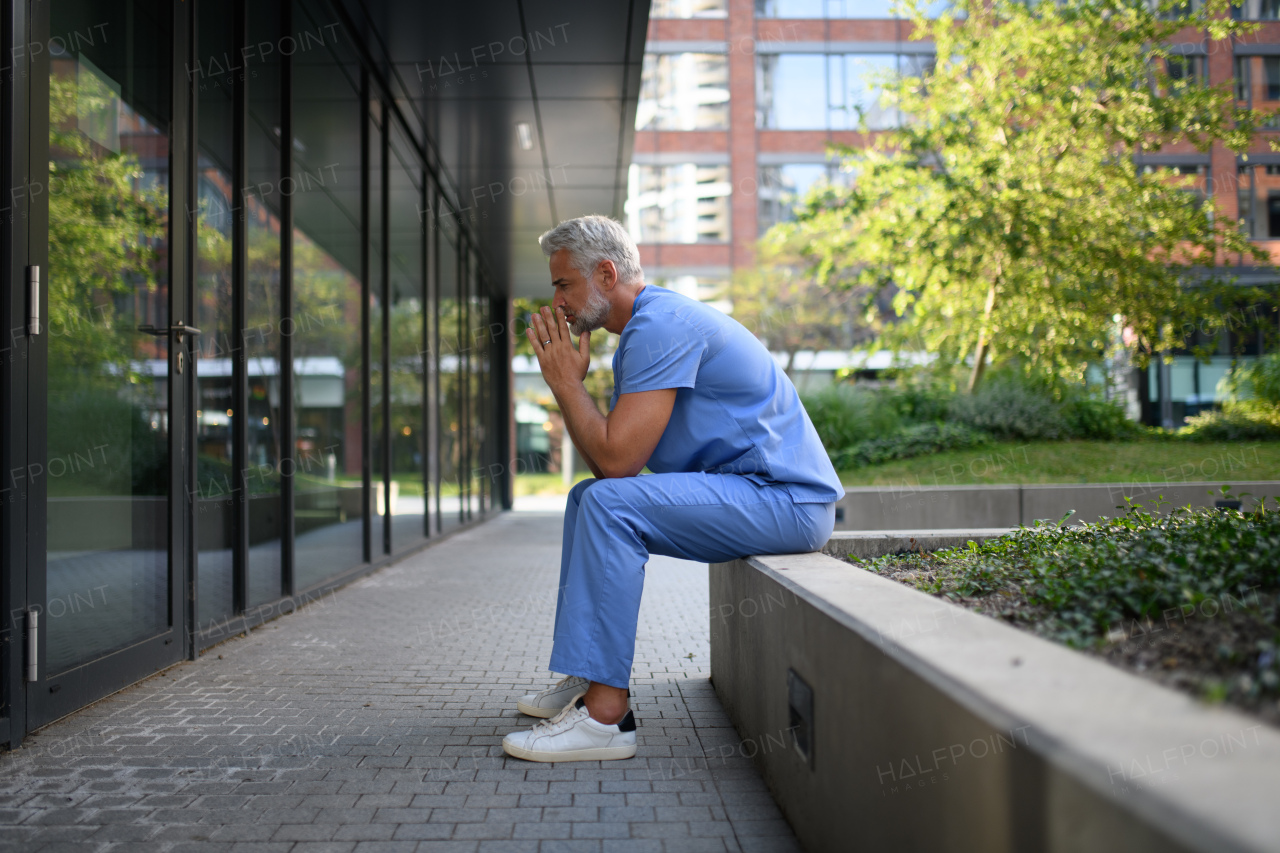 Frustrated and burnt-out doctor standing outside the hospital, feeling down. Mental health problems.